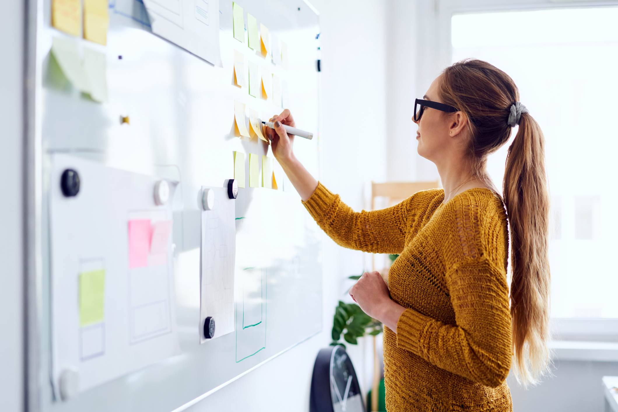 Young-woman-working-in-startup-office-writing-on-whiteboard-how-to-make-an-action-plan-to-achieve-goals