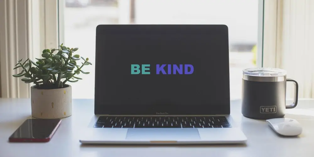 be kind graphic across laptop next to a mug and plant