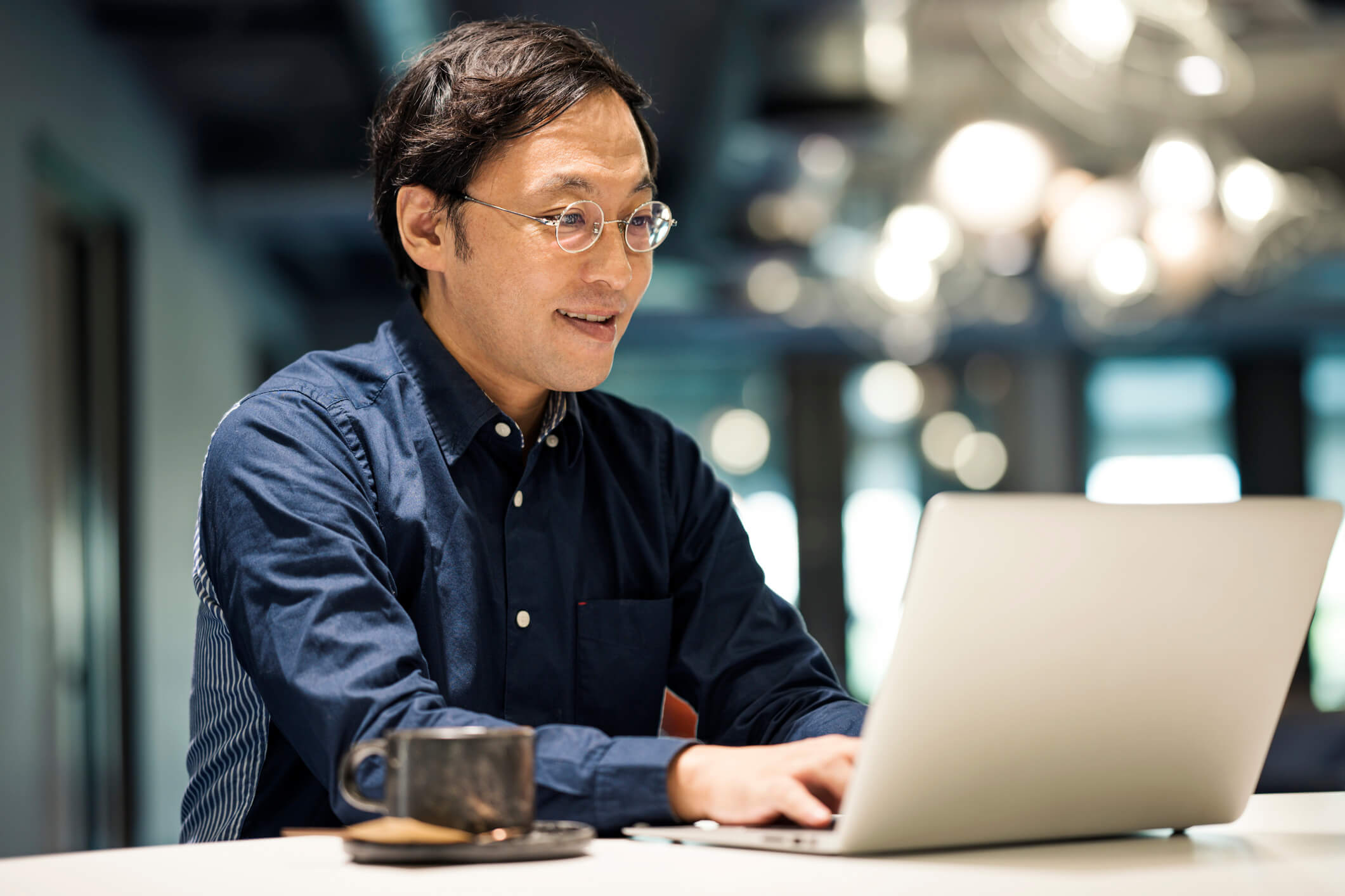 man with glasses and blue shirt typing on laptop