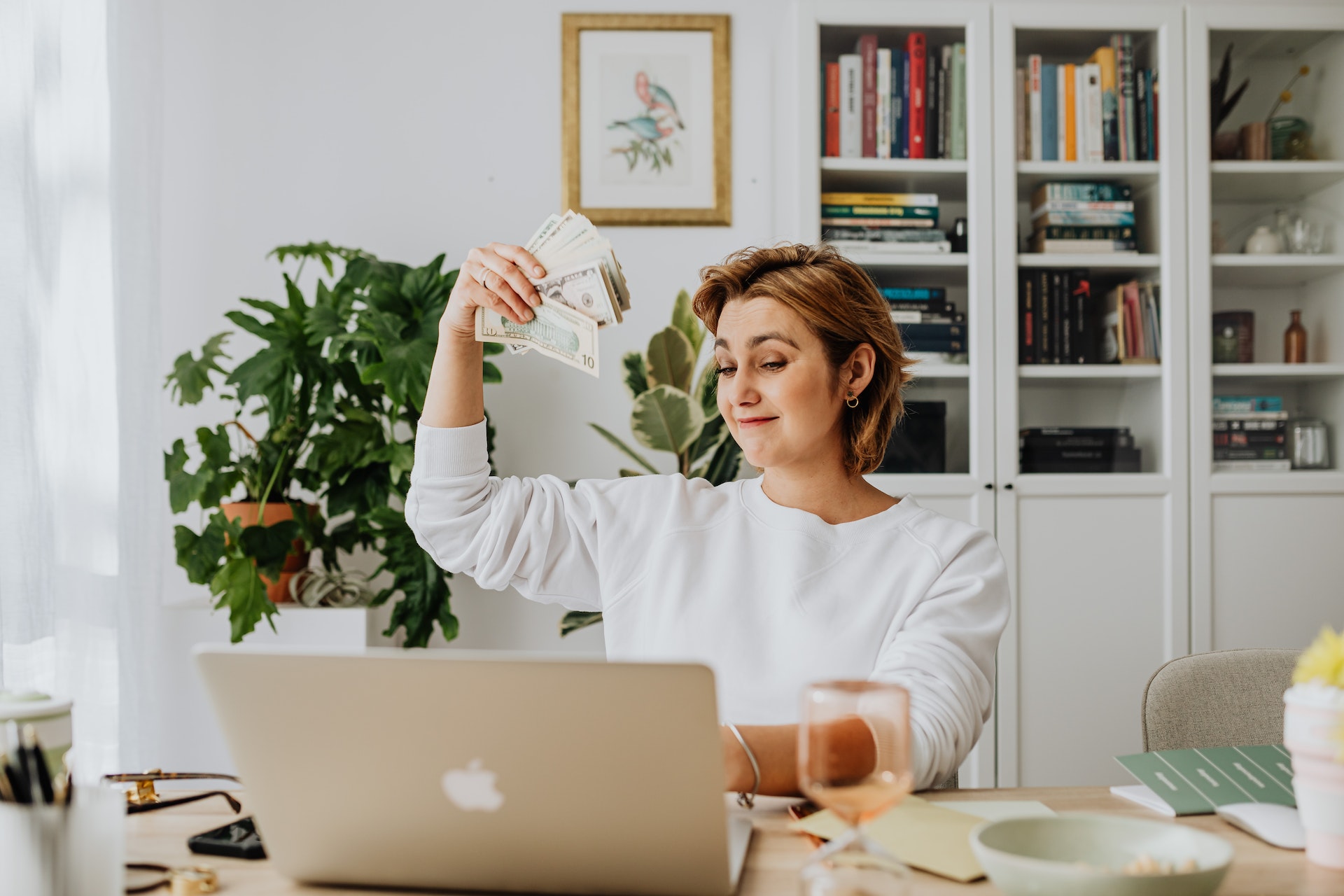 woman-holding-money-in-front-of-a-laptop